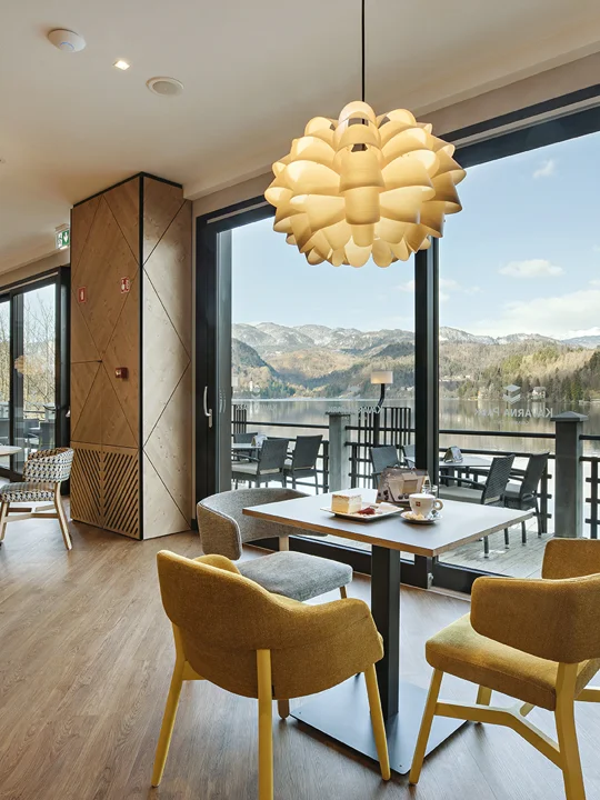 Lepo urejena notranjost hotelske kavarne ob bližini Blejskega jezera s pripravljenimi mizami in rumenimi stoli