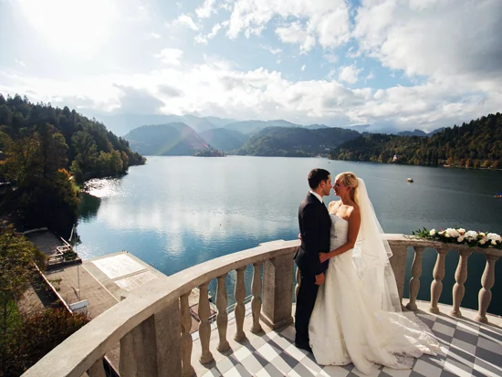 Ženin in nevesta se objemata in stojita na terasi s pogledom na blejsko jezero