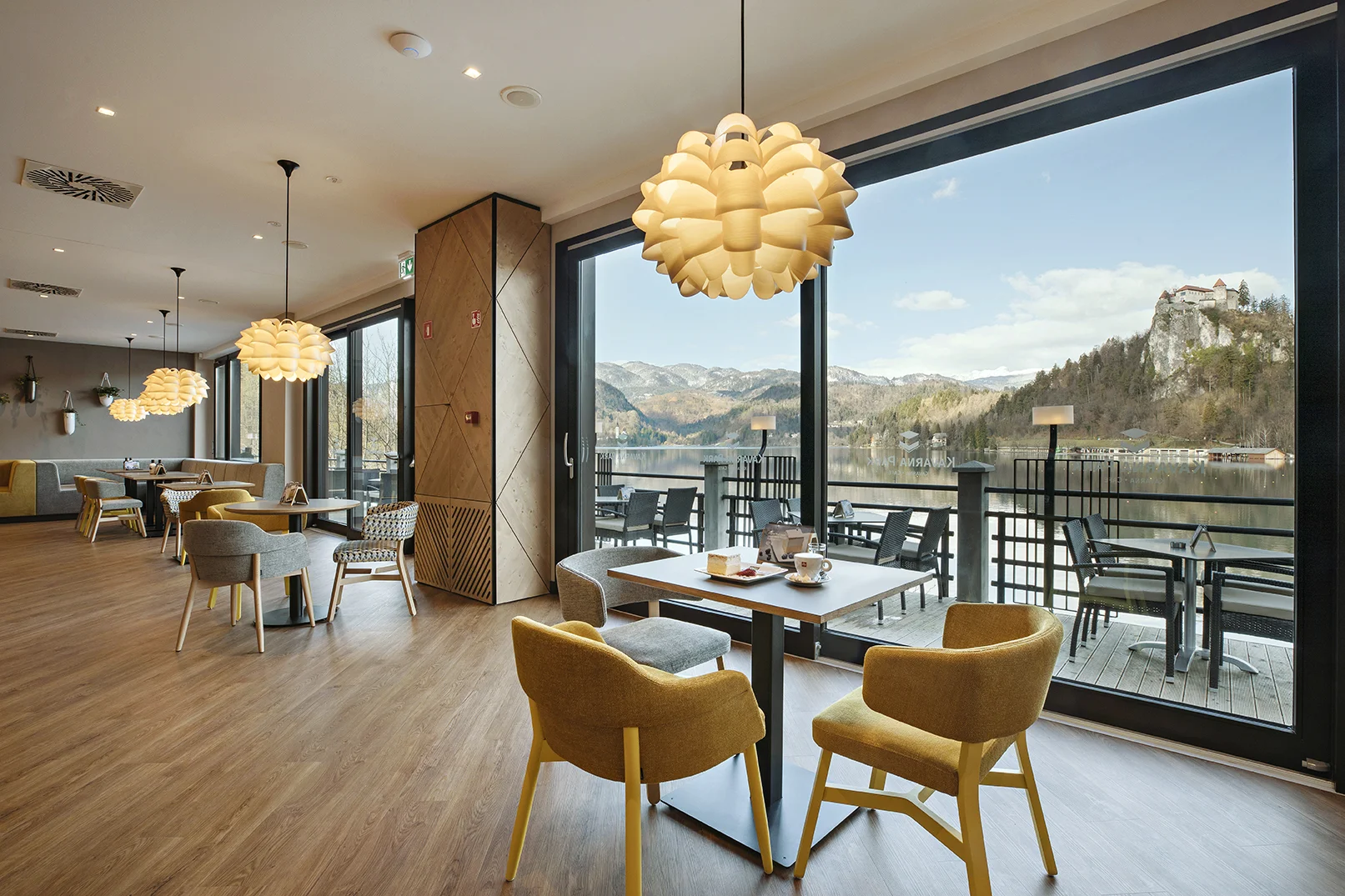 Lepo urejena notranjost hotelske kavarne ob bližini Blejskega jezera s pripravljenimi mizami in rumenimi stoli