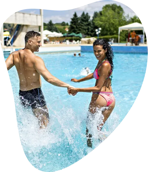 Moški in ženska se nasmejana držita za roke v zunanjem bazenu vodnega parka in tečeta v bazen