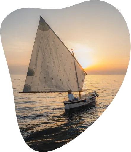 Moški na veliki jadrnici pluje na morju ob sončnem zahodu