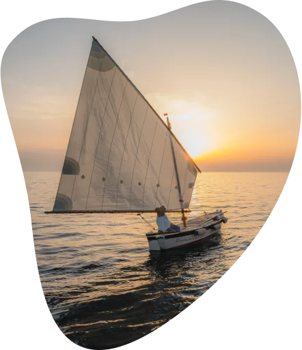 Moški na veliki jadrnici pluje na morju ob sončnem zahodu