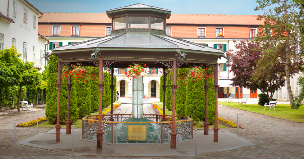 Lepo urejen zelen park z mineralnim vrelcem v ospredju in sprehajalnimi potkami