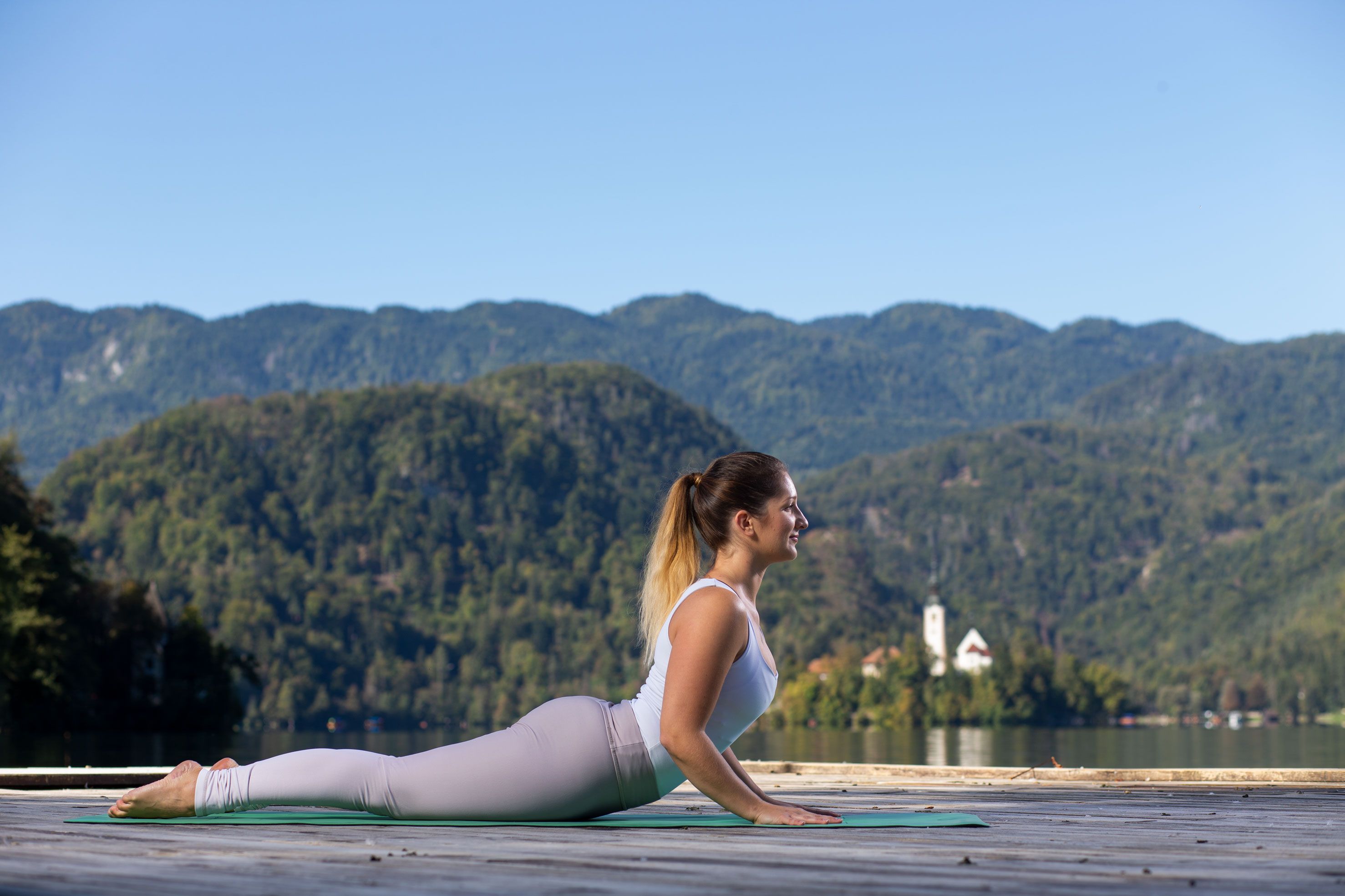 Ženska v športnih oblačilih leži na trebuhu in izvaja jogo ob blejskem jezeru