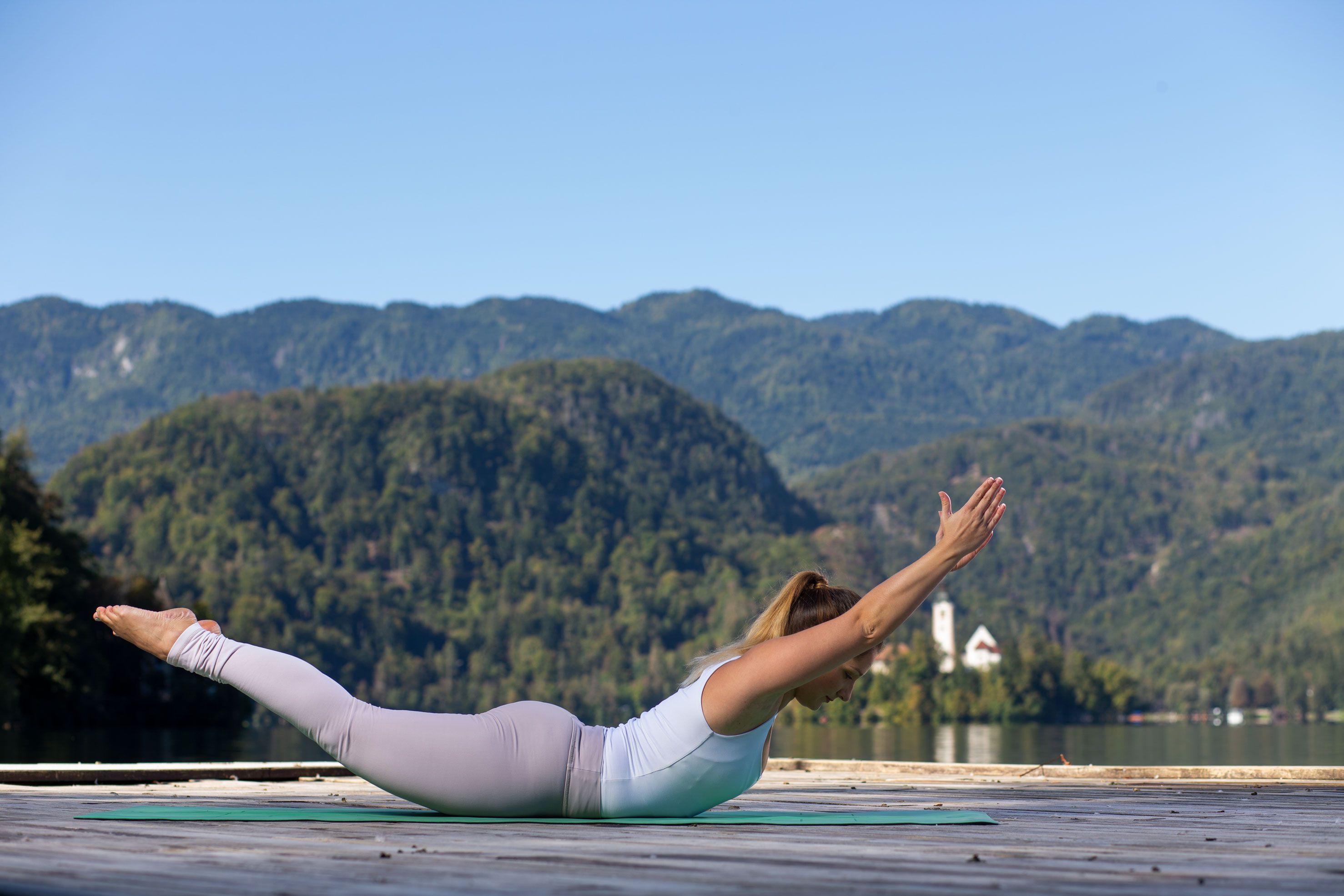 Ženska v športnih oblačilih leži na trebuhu in izvaja jogo ob blejskem jezeru