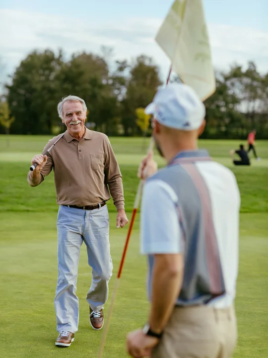 Moški v športnih oblačilih z golf palico v roki se pogovarja z drugim moškim na golf igrišču