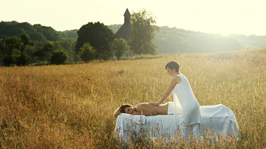 Ženska v beli obleki izvaja masažo hrbta na masažni mizi na travniku