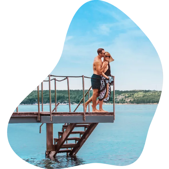 Moški in ženska v kopalkah stojita ob robu pomola ob morju in se objemata