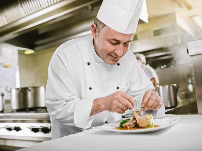 Kuharski mojster Danilo Čurman v kuharskih oblačilih v kuhinji pripravlja jed